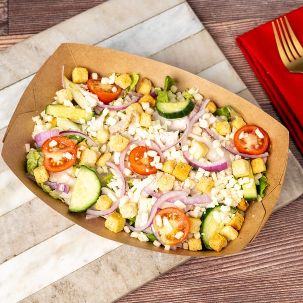 A fresh garden salad with tomatoes, cucumbers, red onions, croutons, and cheese in a brown paper container.