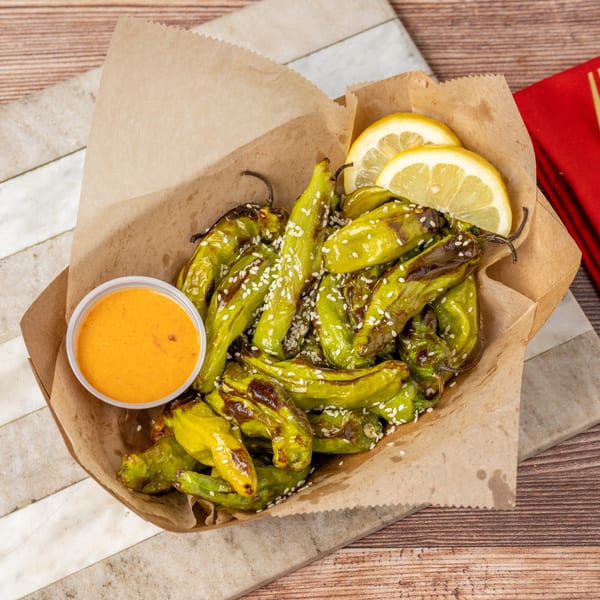 Roasted green peppers with sesame seeds, lemon slices, and a side of orange dipping sauce.