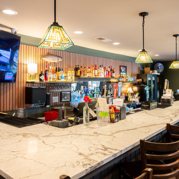 A well-stocked bar with a marble countertop, bar stools, and Tiffany-style pendant lights.
