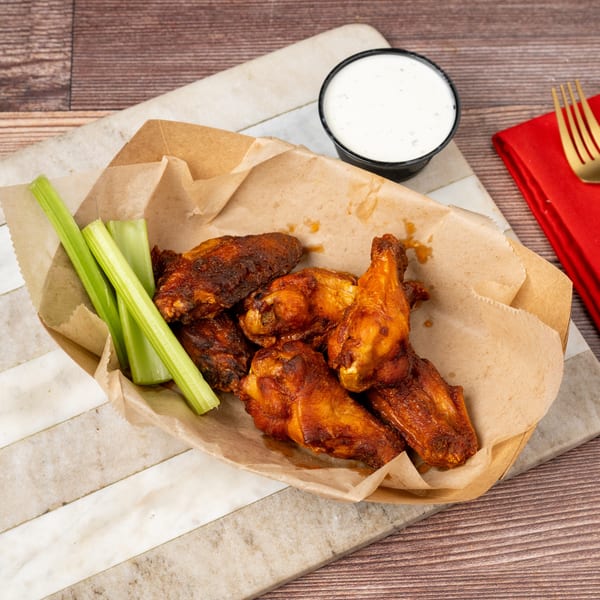Crispy chicken wings with celery sticks and a side of ranch dressing in a paper tray.