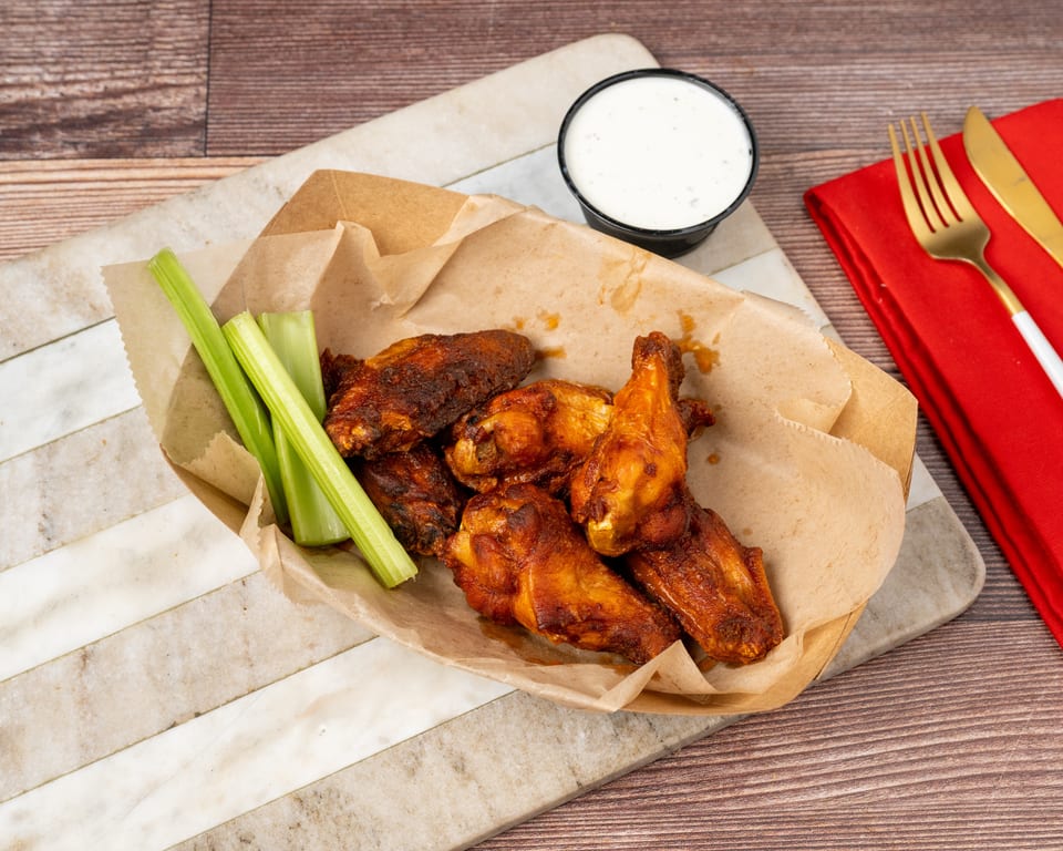 Crispy chicken wings with celery sticks and a side of ranch dressing in a paper tray.