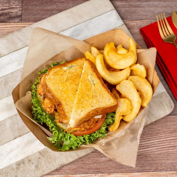 Crispy chicken sandwich with lettuce, tomato, and pickles, served with curly fries in a paper tray.