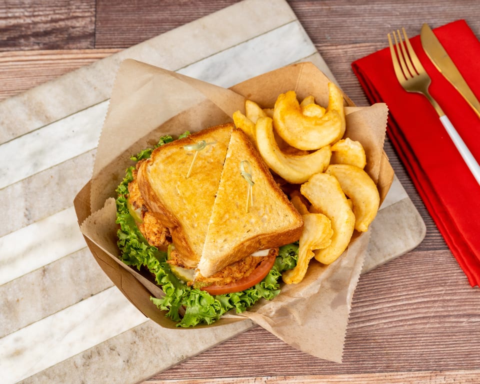 Crispy chicken sandwich with lettuce, tomato, and pickles, served with curly fries in a paper tray.