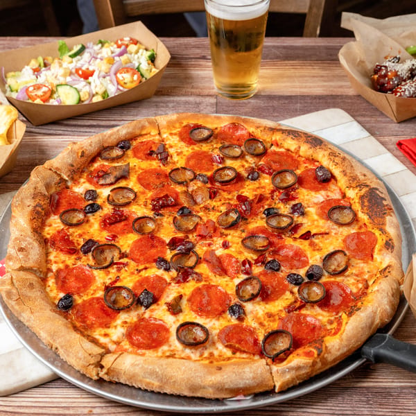 Pepperoni pizza with mushrooms and olives, surrounded by fries, salad, wings, and tater tots.