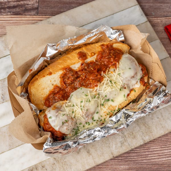 Meatball sub with marinara sauce and melted cheese in a foil-lined paper tray.
