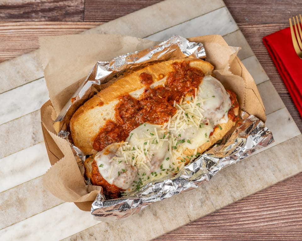 Meatball sub with marinara sauce and melted cheese in a foil-lined paper tray.
