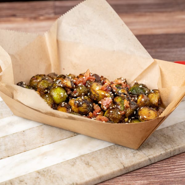Roasted Brussels sprouts with bacon and sesame seeds in a brown paper serving tray.