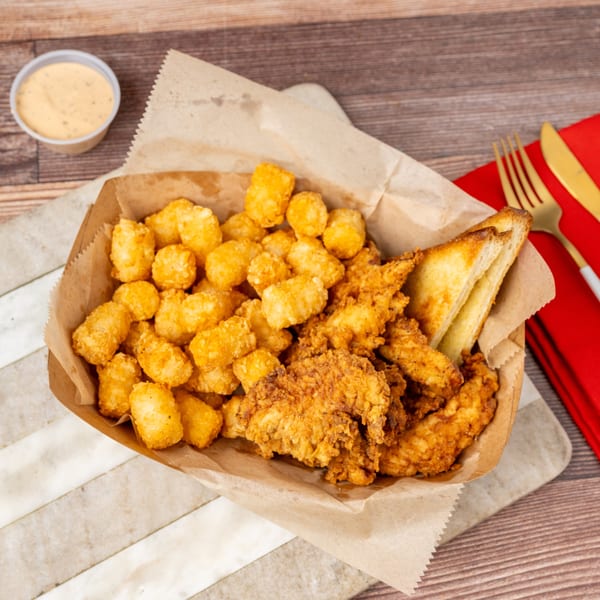 Fried chicken tenders, tater tots, and Texas toast in a paper-lined basket with dipping sauce.