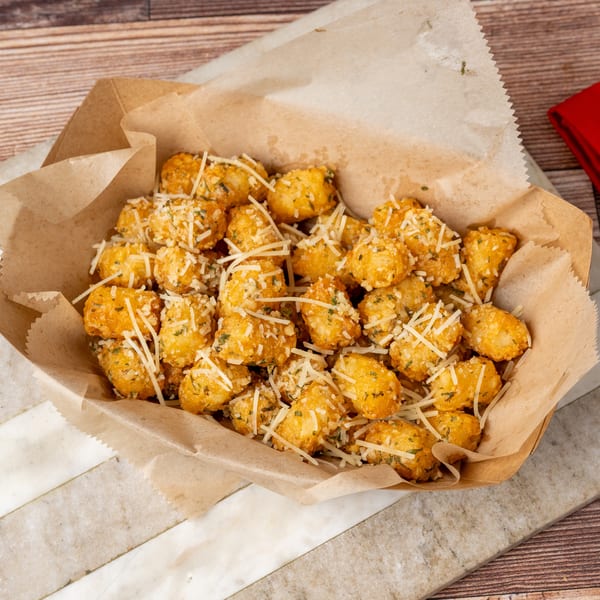 Golden tater tots topped with shredded cheese and herbs in a brown paper container.