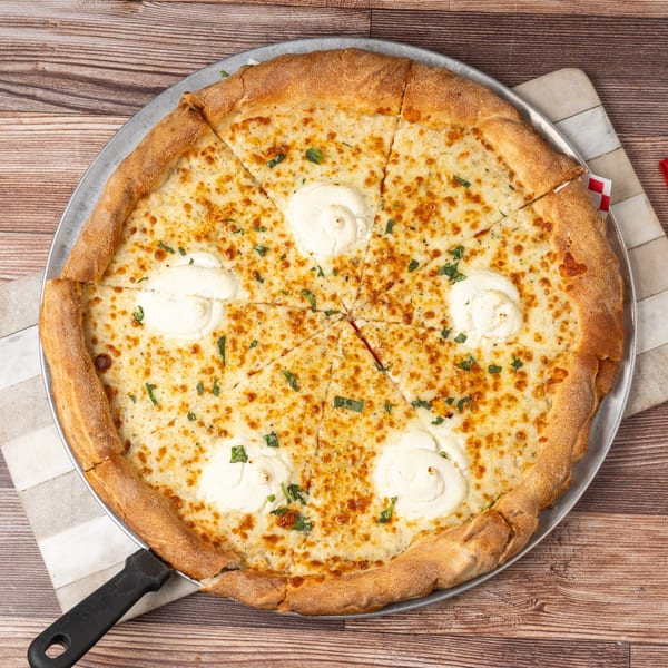 A white pizza with dollops of ricotta cheese and fresh basil on a wooden table.