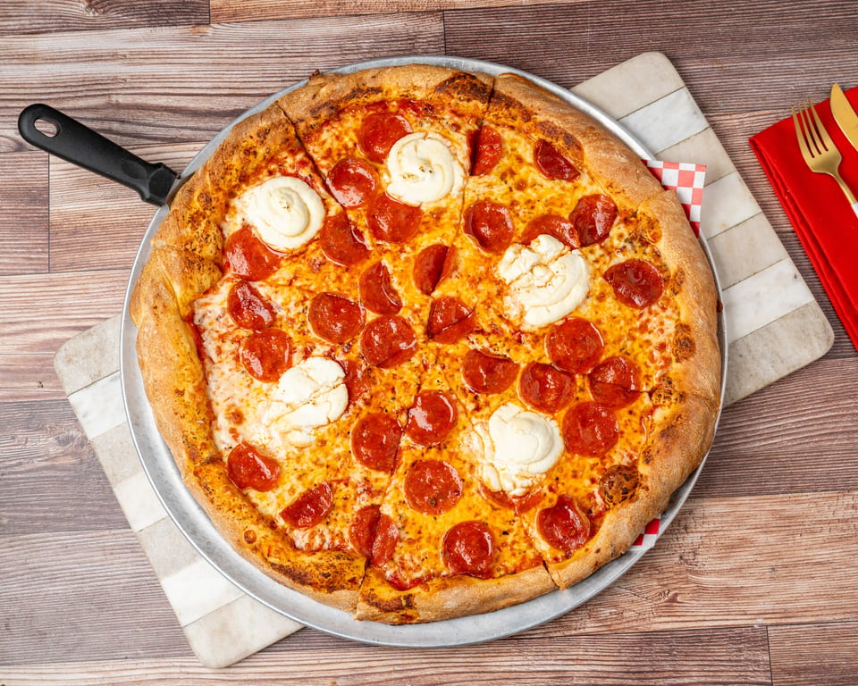 Pepperoni and ricotta cheese pizza on a metal pan with a red napkin and gold fork.