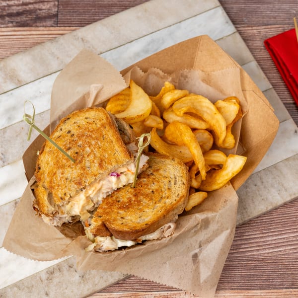 Grilled sandwich with coleslaw and fries in a paper tray, on a marble and wood surface.