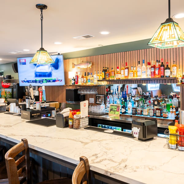 A well-stocked bar with various liquor bottles, a TV, and wooden bar stools.