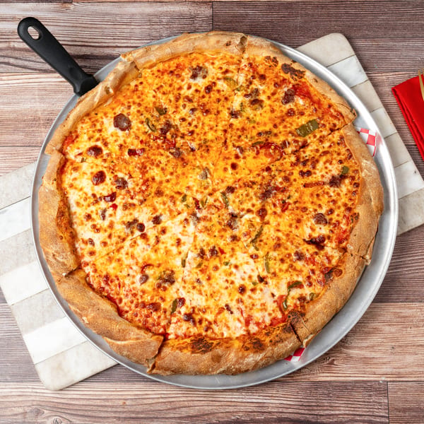 A large, sliced pizza with melted cheese, sausage, and green peppers on a metal pan.
