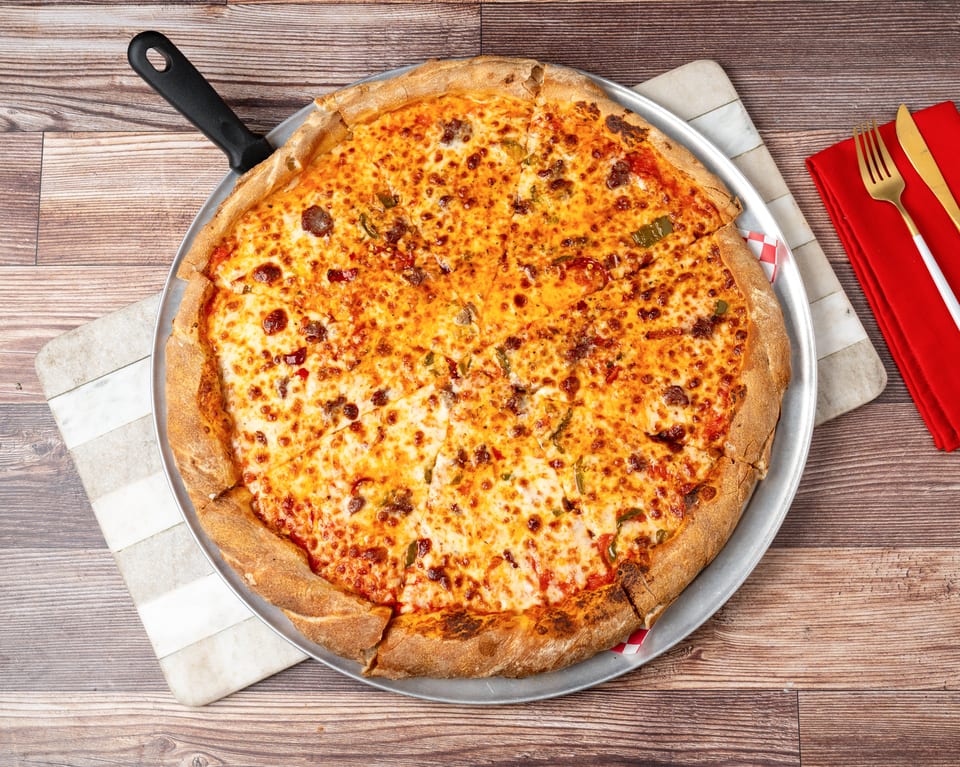 A large, sliced pizza with melted cheese, sausage, and green peppers on a metal pan.